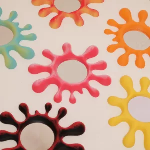 Collection colorée de miroirs SLPAT! en forme d'éclaboussures, déclinés en plusieurs teintes vibrantes comme le jaune banane, le rouge fraise-citron et le vert menthe-citron, disposés sur une surface claire